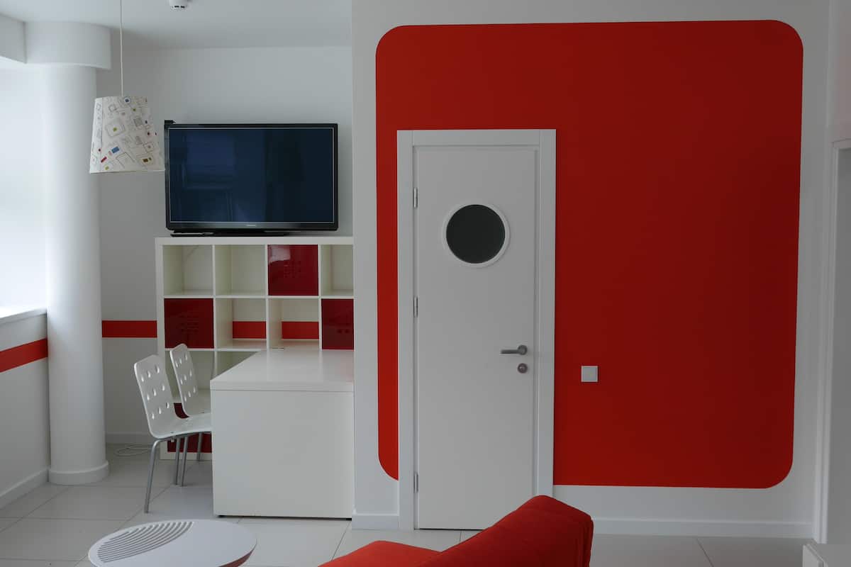 A modern room with a TV on a white stand, a red door, and a white chair.