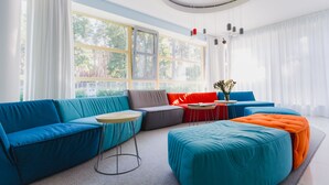 Una sala de estar moderna con sofás azul turquesa y naranja, una mesa de centro redonda y ventanas amplias con cortinas.