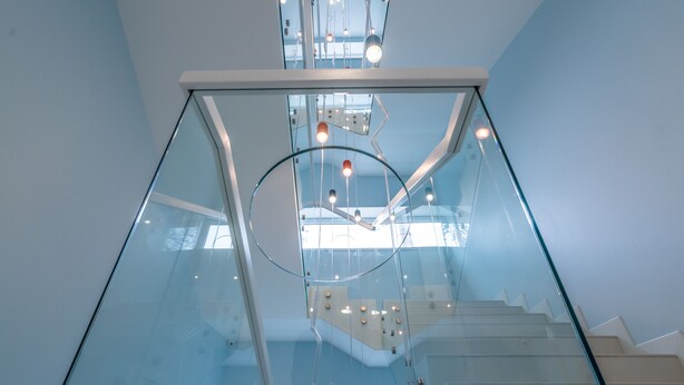 Un interior moderno con una escalera de cristal, barandillas de metal e iluminación expuesta en el techo.