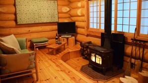 Un interior acogedor de cabaña de madera con un sofá de madera, una mesita, un televisor y una estufa de leña.