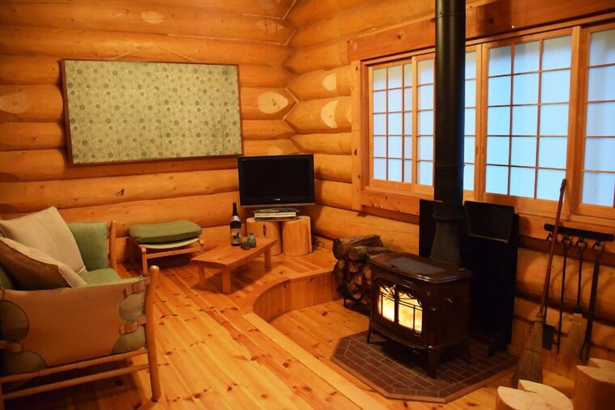 Un interior acogedor de cabaña de madera con un sofá de madera, una mesita, un televisor y una estufa de leña.
