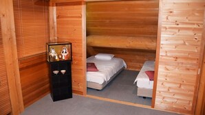 Una habitación de cabaña de madera con dos camas, una estantería decorada y un ventanal con persianas.