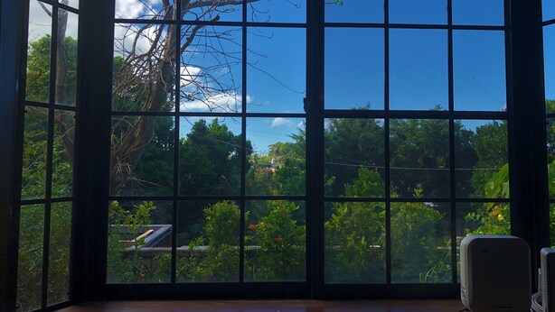Habitación con un amplio ventanal que ofrece vistas a árboles y un cielo despejado.