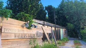 Un letrero de madera para un hotel privado llamado 'WALKERS NAKIJIN', con un diseño rústico y una escalera metálica que conduce a un edificio con grandes ventanales.