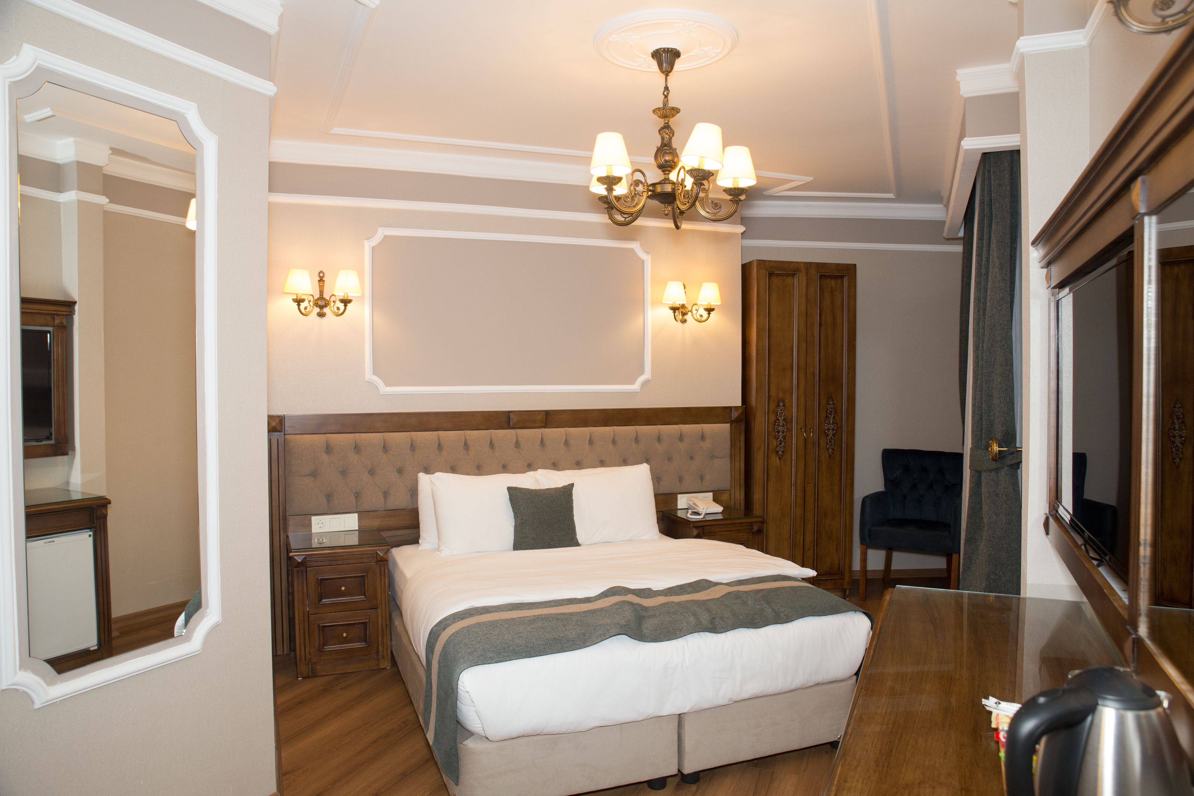 Habitación de hotel con una cama grande, cabecera de madera, candelabro, espejo y escritorio con teléfono.