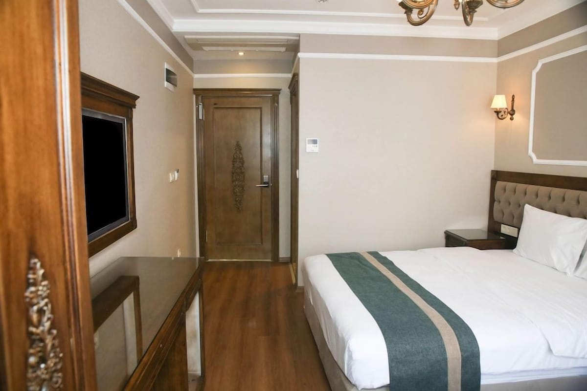 A hotel room with a bed, bedside tables, a television, and a door leading to another room.