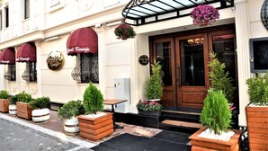 L’entrée d’un hôtel, avec un auvent en verre, des plantes en pot et une porte en bois.