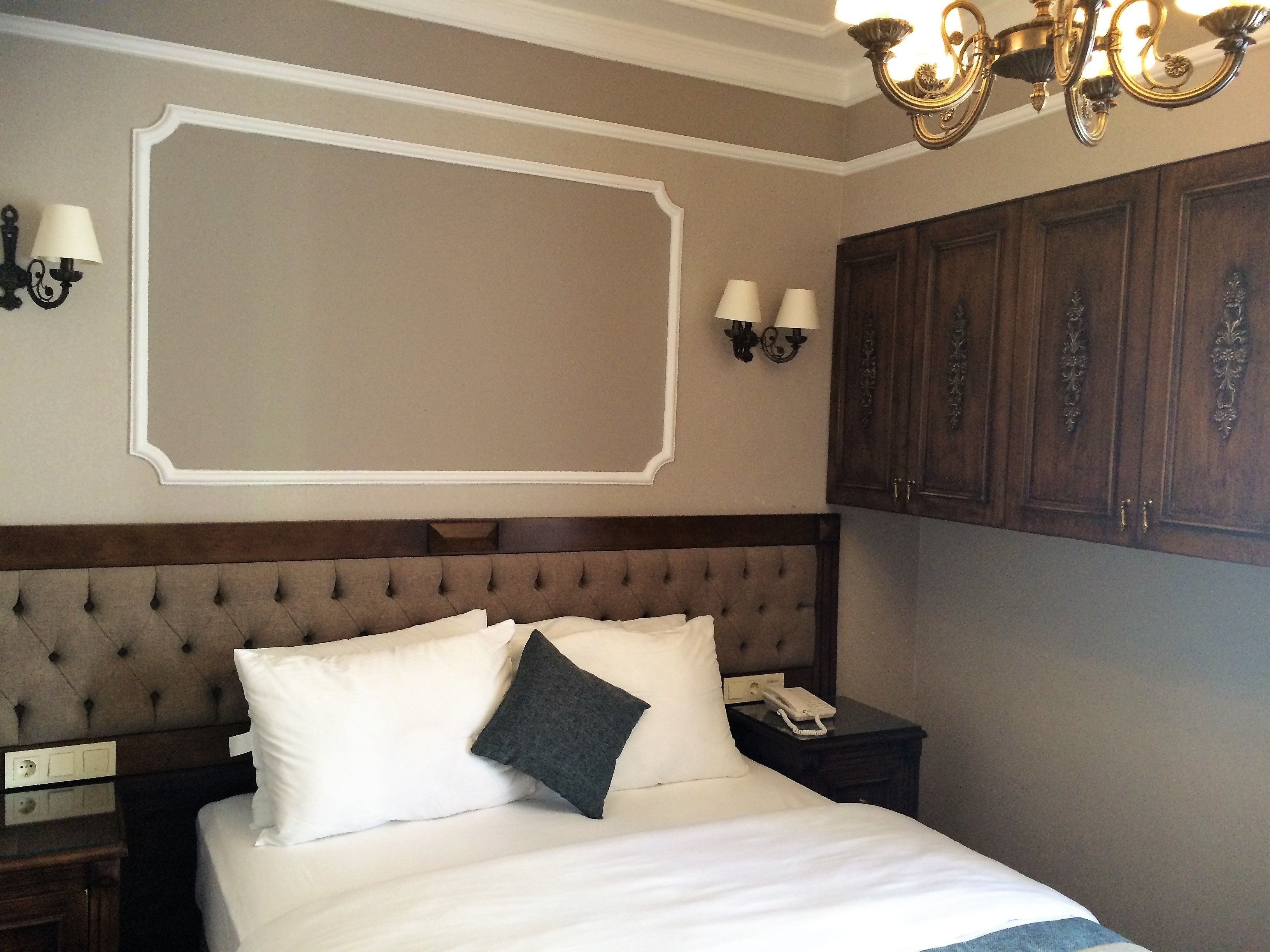 A neatly made bed with a tufted headboard, two bedside lamps, a telephone, and a wall-mounted light fixture.