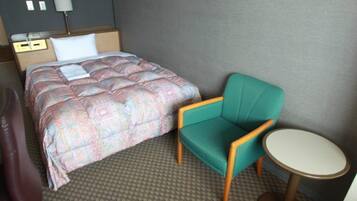 A hotel room with a bed, a chair, a small table, and a lamp.