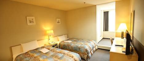 Una habitación de hotel con dos camas, un escritorio con computadora y una ventana con cortinas.