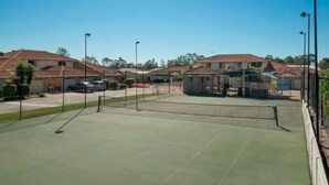 A tennis court surrounded by residential buildings with a clear sky. - Huntington Villas (Warner)