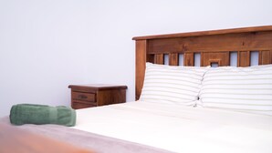 A neatly made bed with striped pillows and a wooden headboard, a small wooden nightstand with a drawer, and a green towel on the bed. - Huntington Villas (Warner)