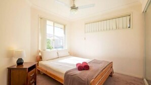A bedroom with a single bed, a nightstand, a ceiling fan, and a window with blinds. - Huntington Villas (Warner)