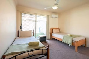 A room with two single beds, a ceiling fan, and a sliding glass door leading to an outdoor area. - Huntington Villas (Warner)