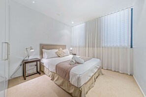 Une chambre à coucher bien rangée, avec un lit, une table de chevet, une lampe et des rideaux.