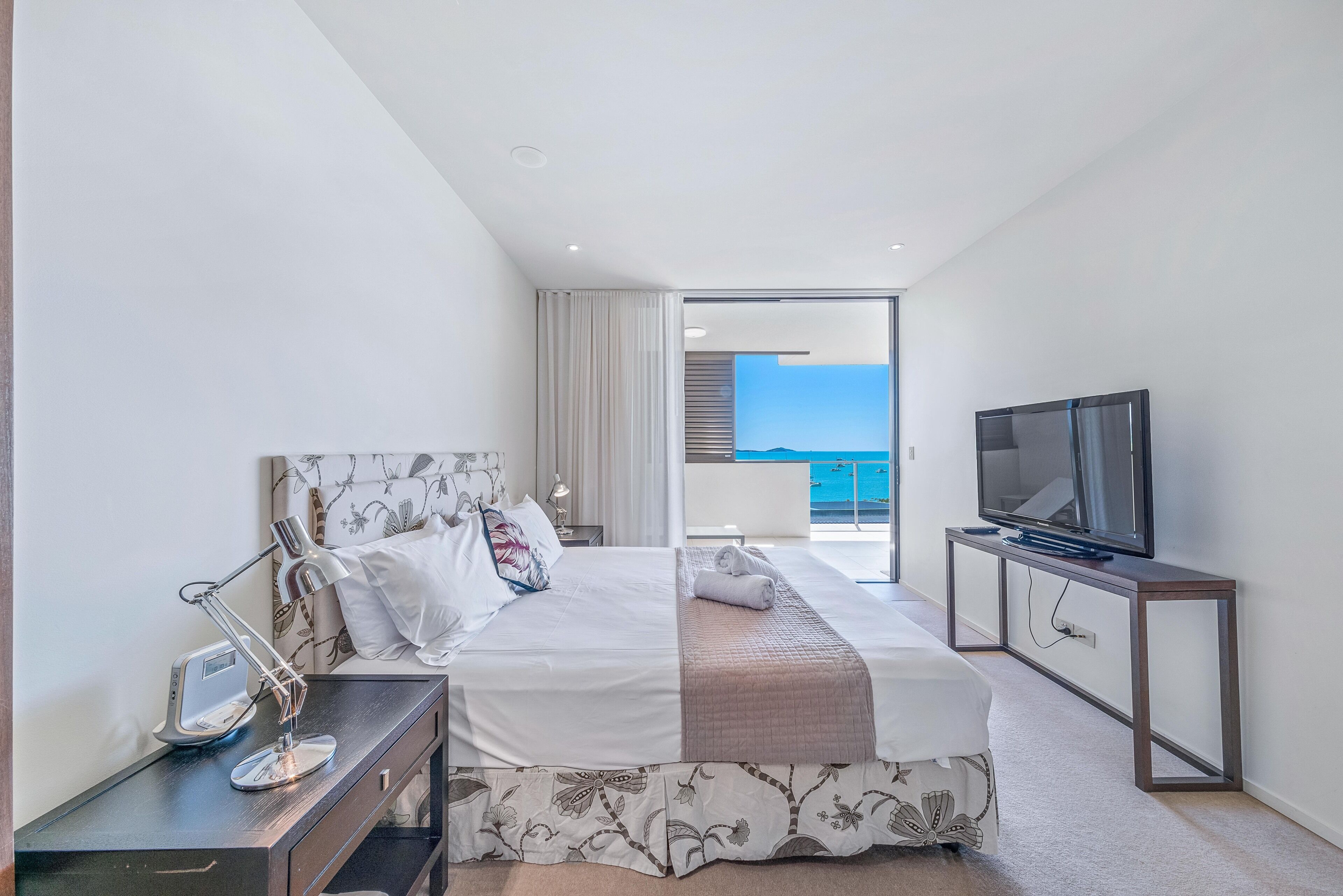 A modern hotel room with a large bed, a TV, and a balcony with a view.