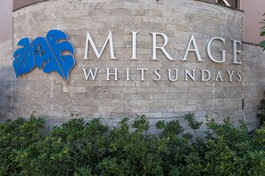 Une enseigne pour « Mirage Whitsundays », avec un logo bleu et du texte, sur un mur de pierre.