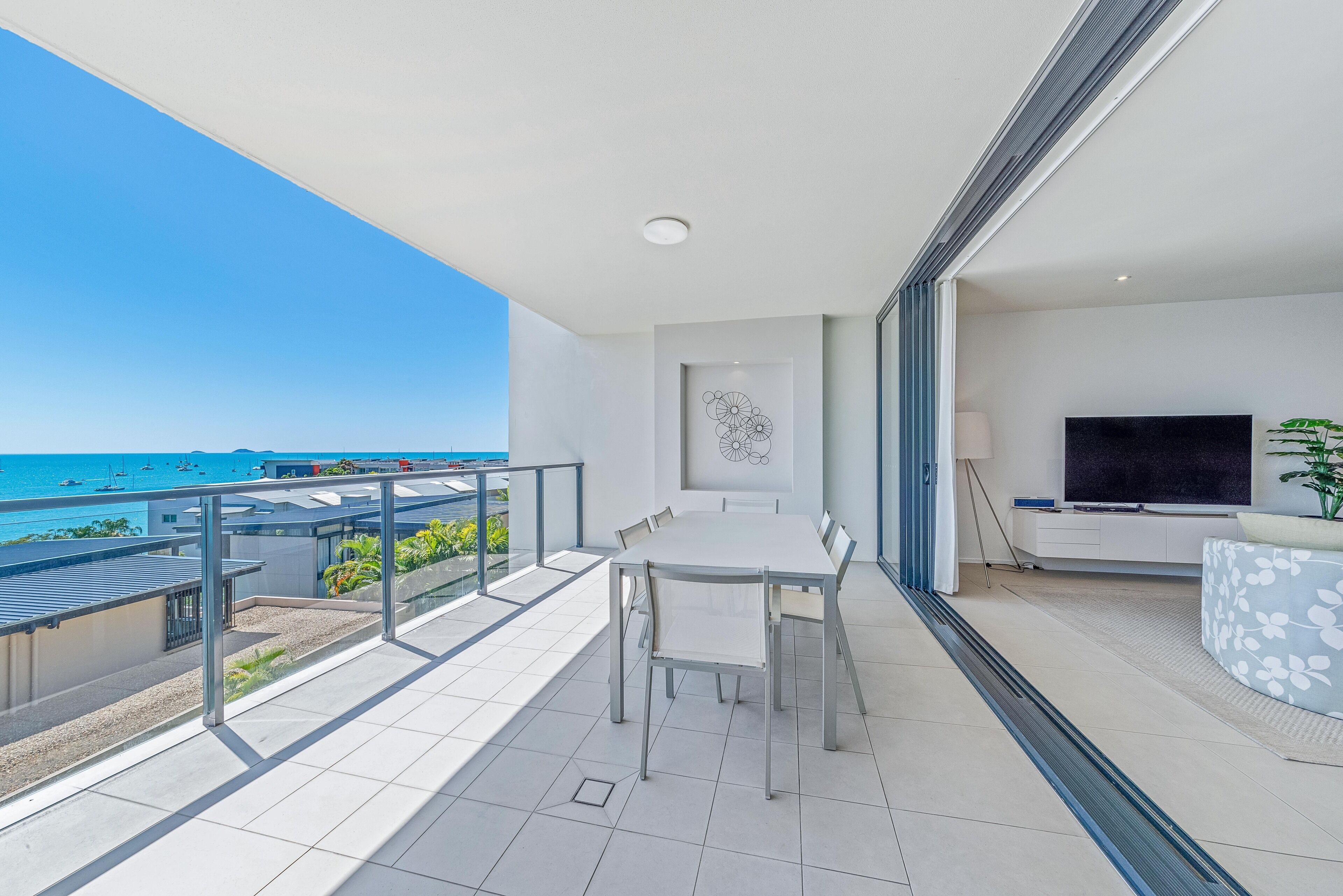 Een balkon met een eettafel en stoelen, een televisie en een decoratief wandobject.