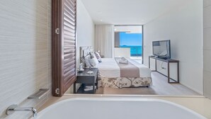 Een moderne hotelkamer met een groot bed, een televisie, een bureau en uitzicht op zee.