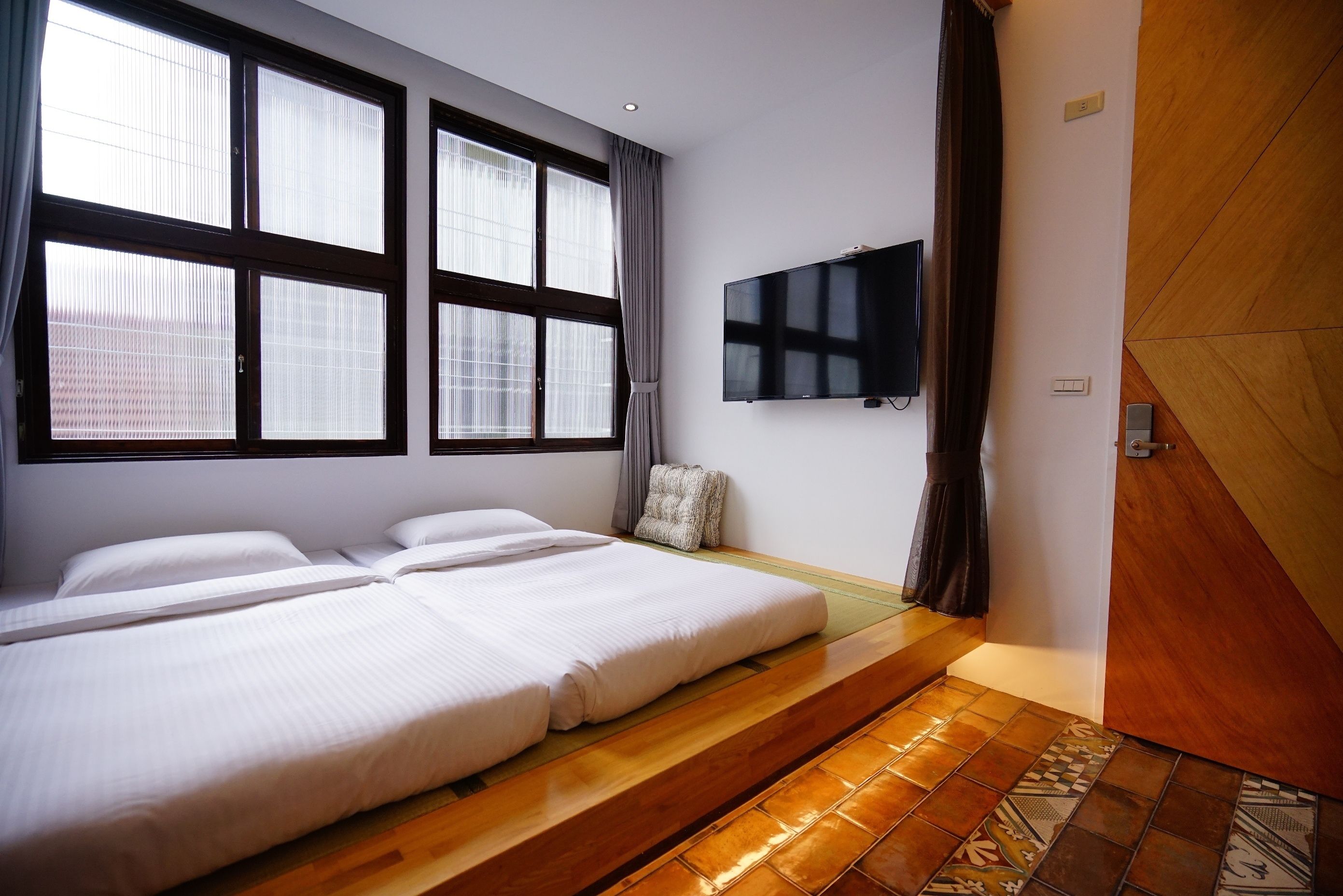 A hotel room with two beds, a TV, large windows, and a wooden floor.