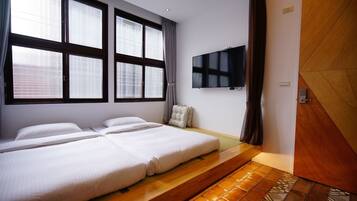 A hotel room with two beds, a TV, large windows, and a wooden floor.