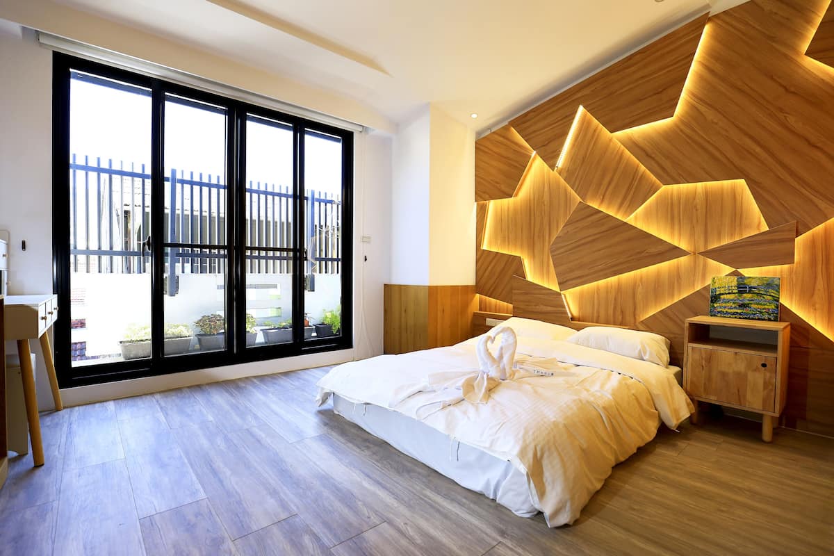 A modern bedroom with a large window, a wooden headboard, and a neatly made bed.