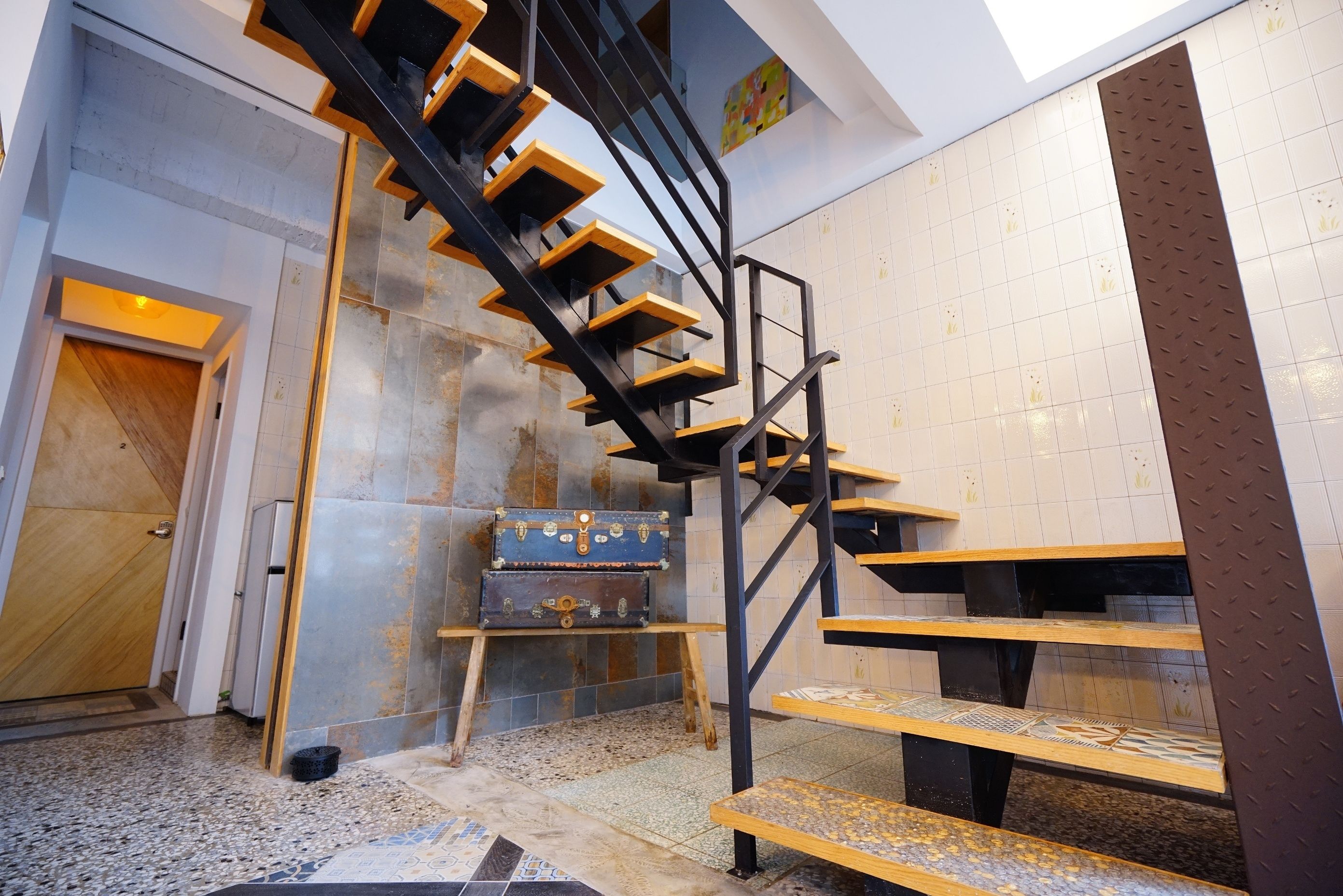 Un interior moderno con una escalera espiral negra, una puerta de madera y una pared de azulejos con un panel decorativo.
