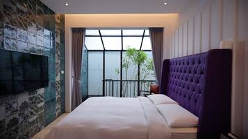 A modern hotel room with a large bed, a flat-screen TV mounted on the wall, a balcony with a view, and a purple headboard.