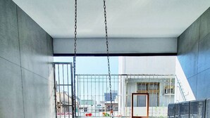 Una habitación con una silla colgante, vistas a edificios y un balcón con una reja de metal.