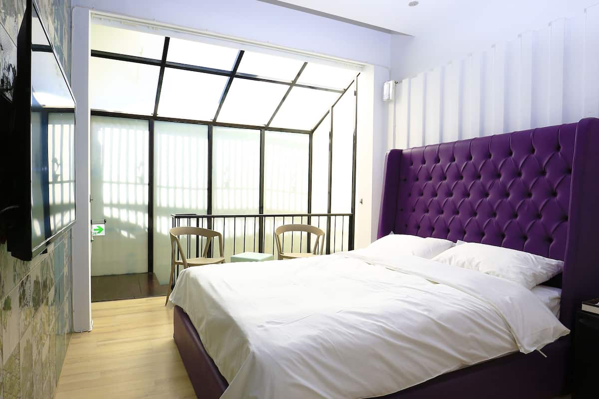 A bedroom with a large bed, a TV mounted on the wall, and a balcony with chairs.