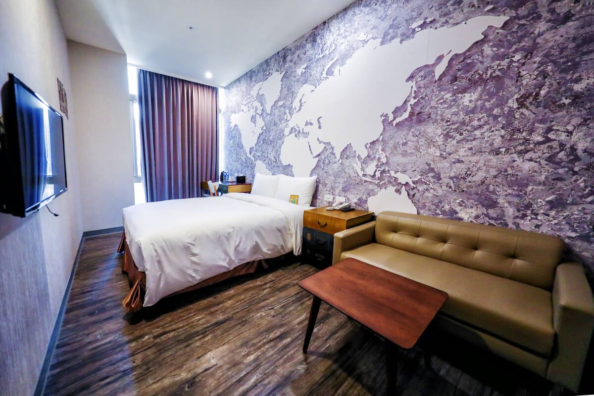 Una habitación de hotel con una cama grande, un sofá, suelo de madera, un mural de un mapa mundial y un televisor de pantalla plana.
