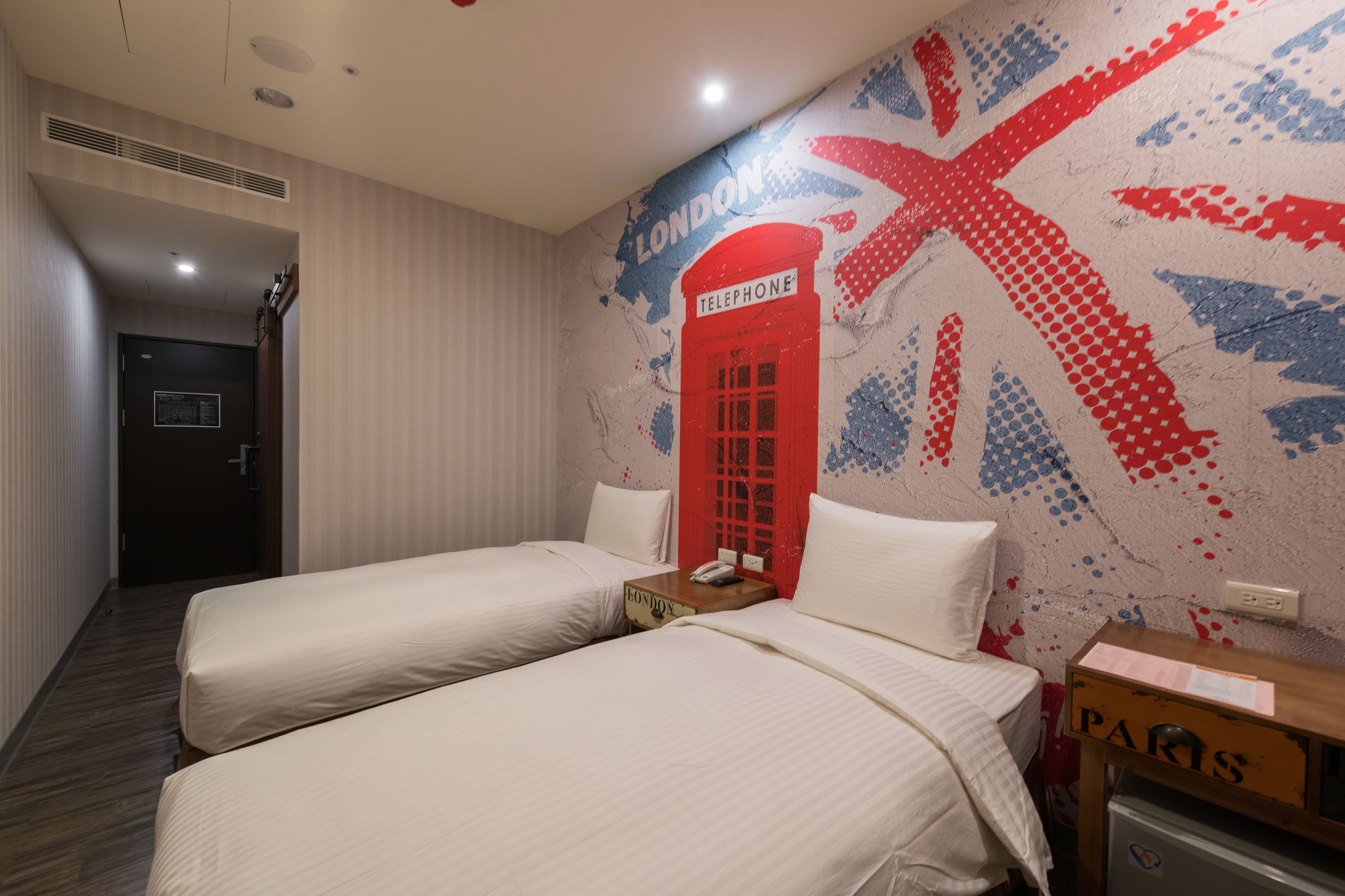 Habitación de hotel con dos camas, un teléfono rojo y un mural en la pared con la bandera del Reino Unido.