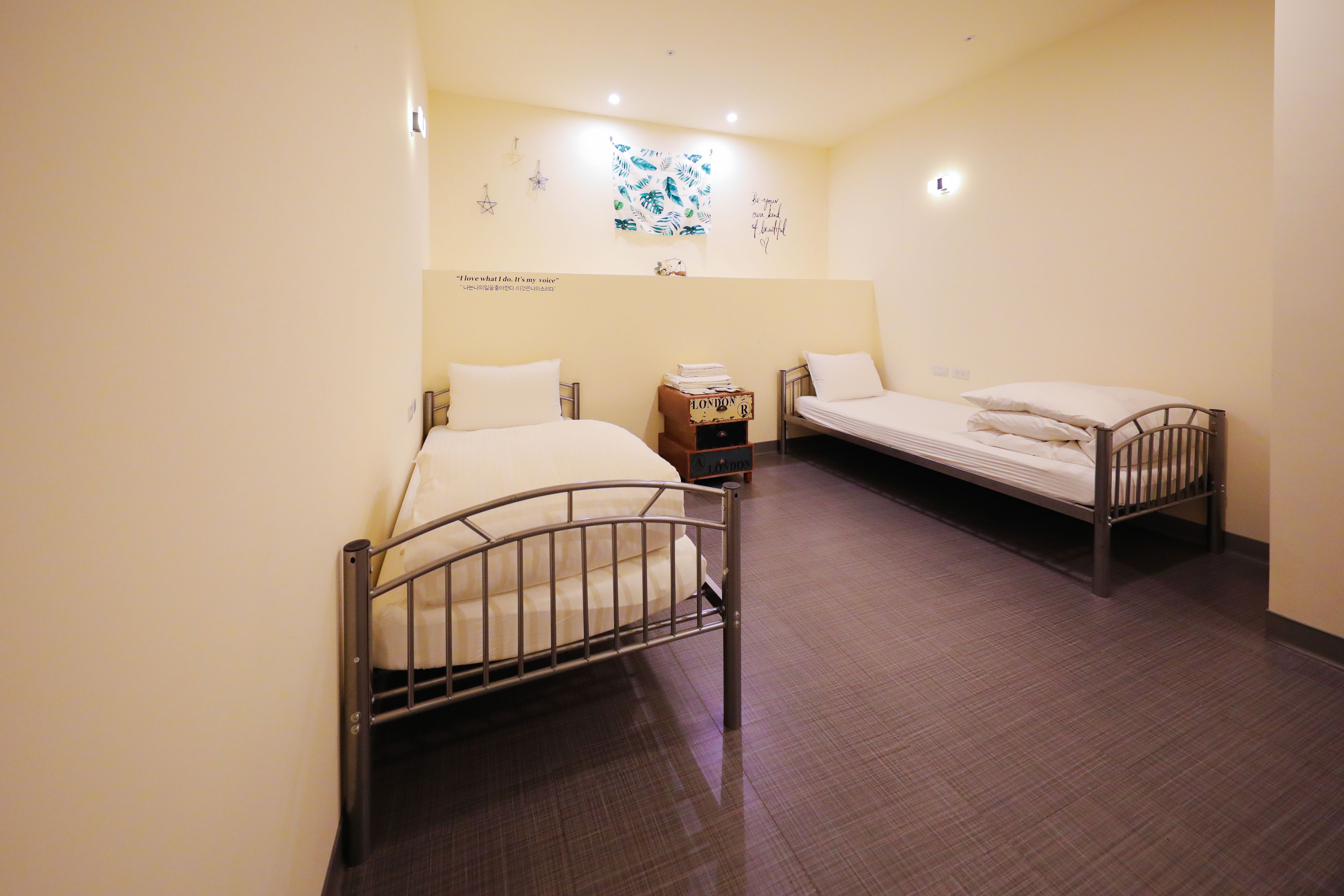 Une chambre avec deux lits simples, une petite table de chevet en bois et un mur agrémenté d’éléments décoratifs.
