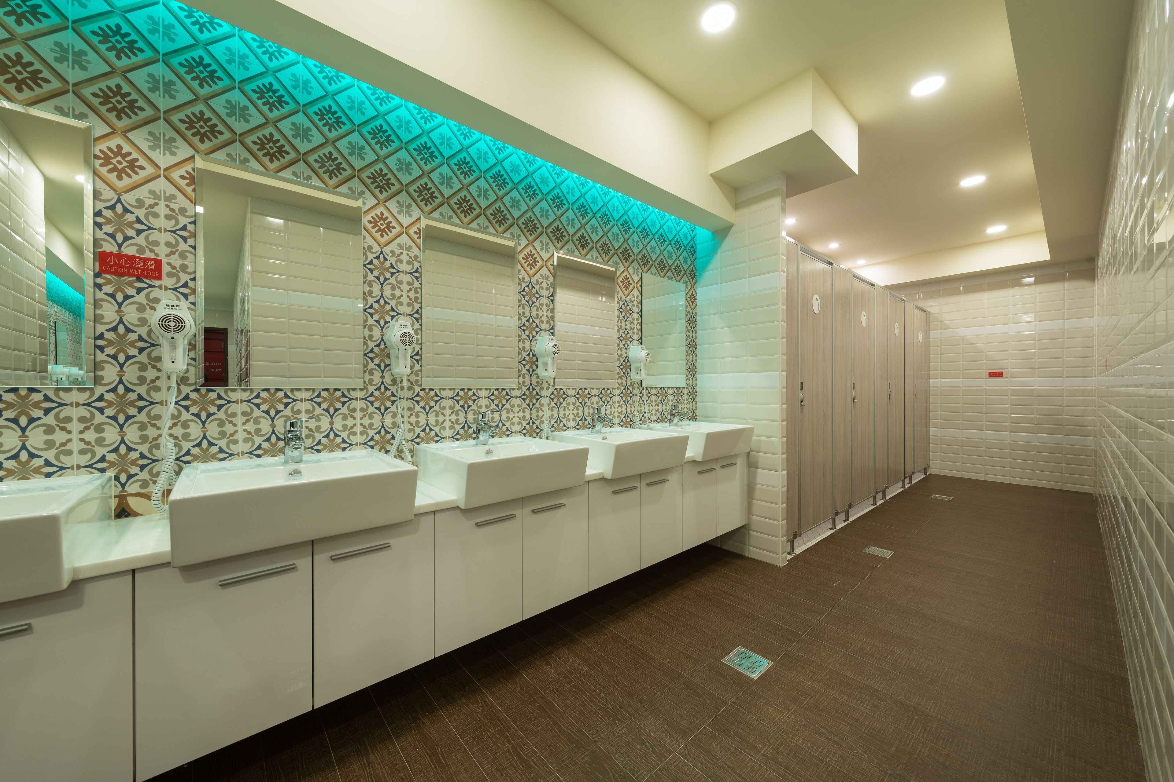 A long, narrow bathroom with multiple sinks and mirrors, tiled walls, and a patterned ceiling.