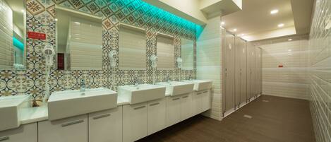 A long, narrow bathroom with multiple sinks and mirrors, tiled walls, and a patterned ceiling.