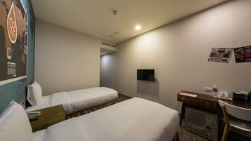 A hotel room with two beds, a desk, a chair, a TV, and a refrigerator.