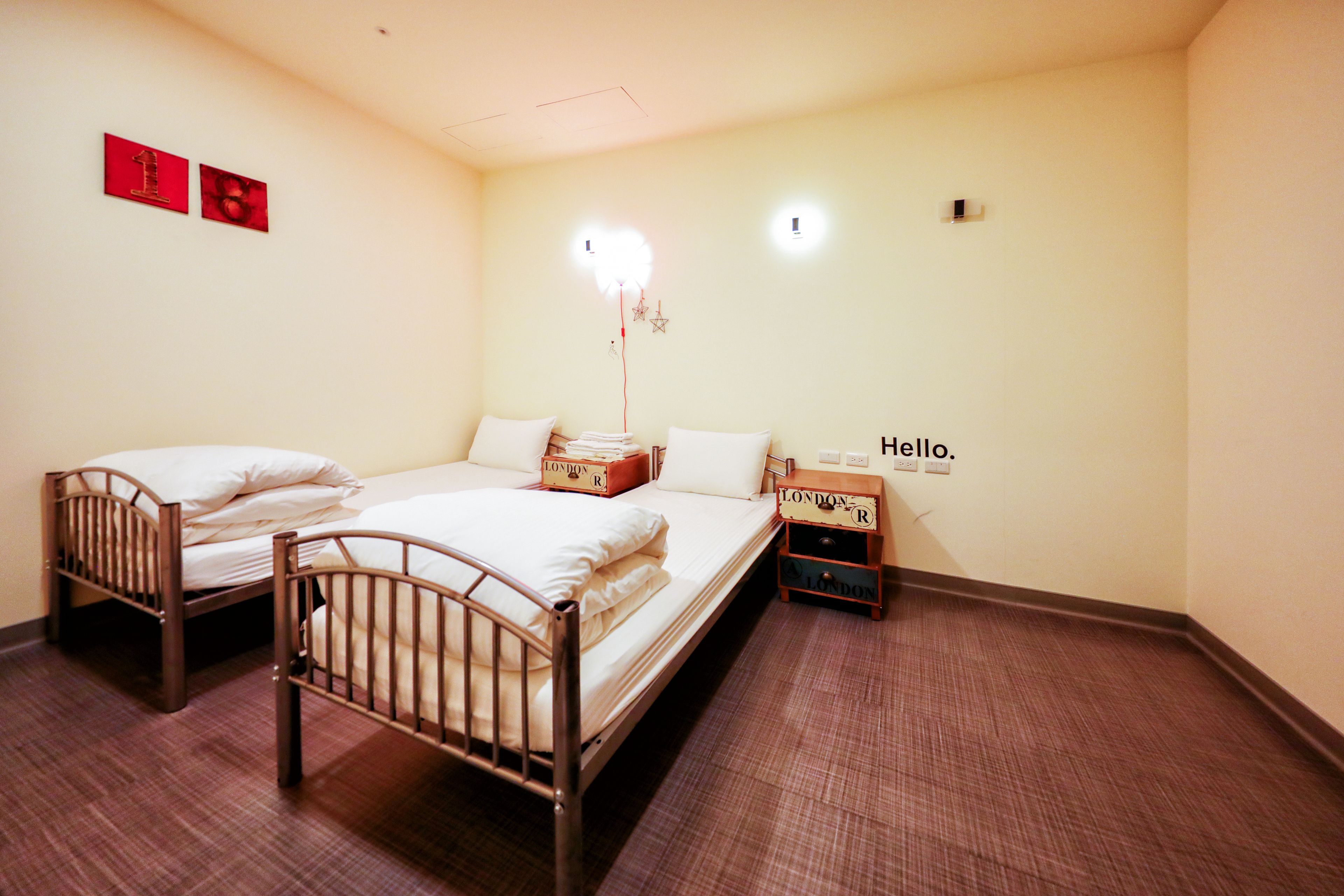 Habitación de hotel con dos camas individuales, una mesita de noche con lámpara y una lámpara de pared.