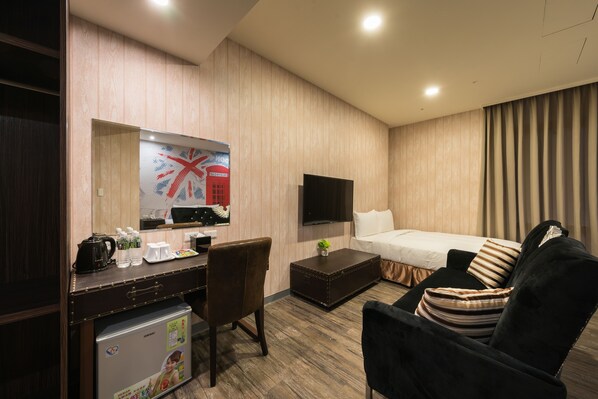 A hotel room with a wooden panel wall, a flat-screen TV, a bed with a striped pillow, a black armchair, a small table with a plant, and a desk with a kettle and water bottles. - Skyone Hotel (Kaohsiung)