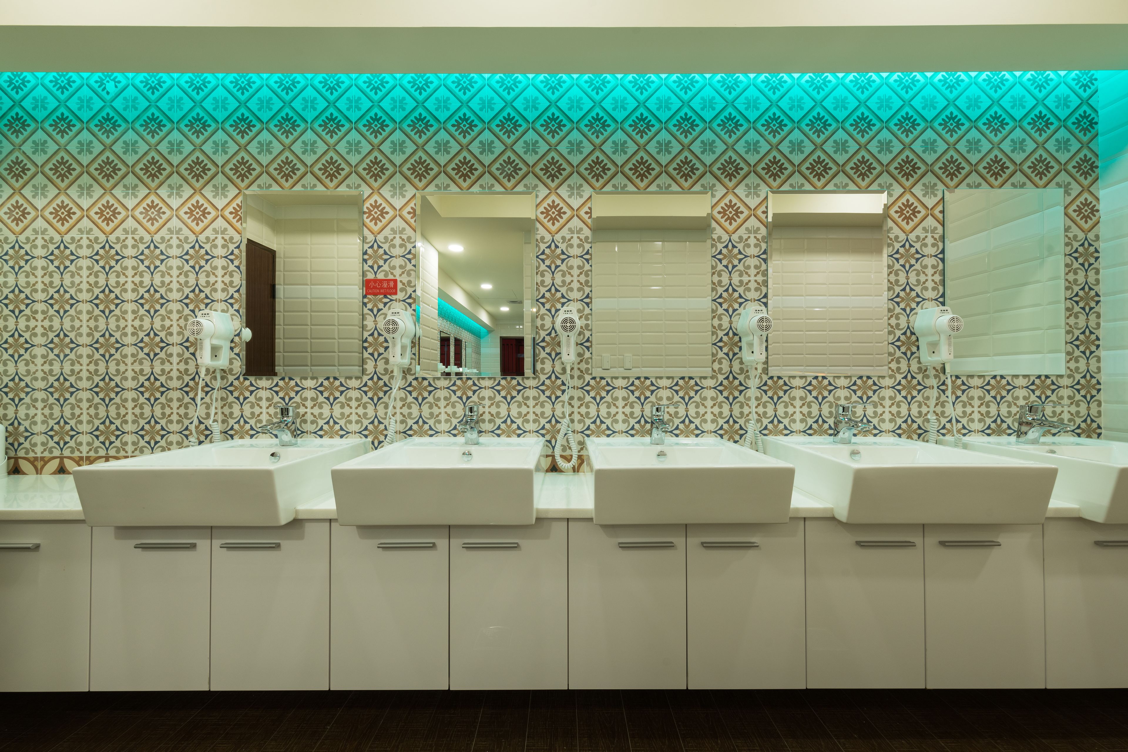 A bathroom with three sinks, white cabinets, and patterned tiles.