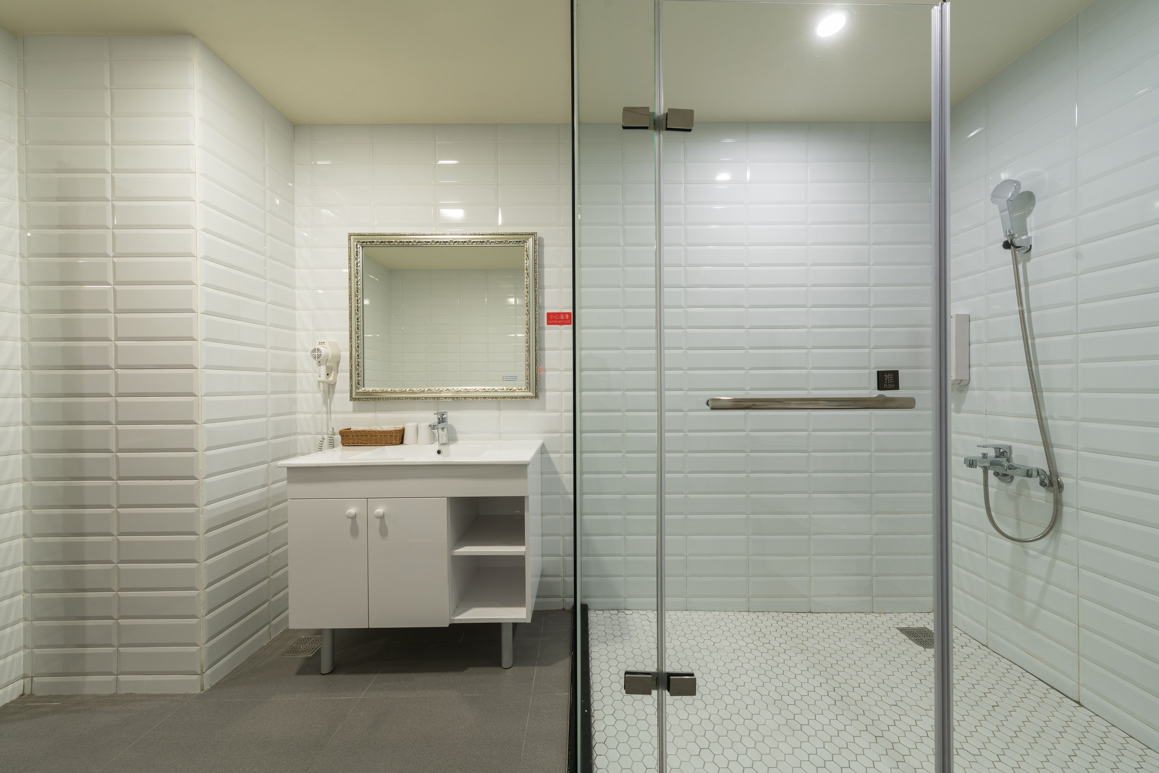 Une salle de bain moderne avec des murs recouverts de carreaux blancs, une douche à parois de verre et un meuble-lavabo blanc avec un miroir.