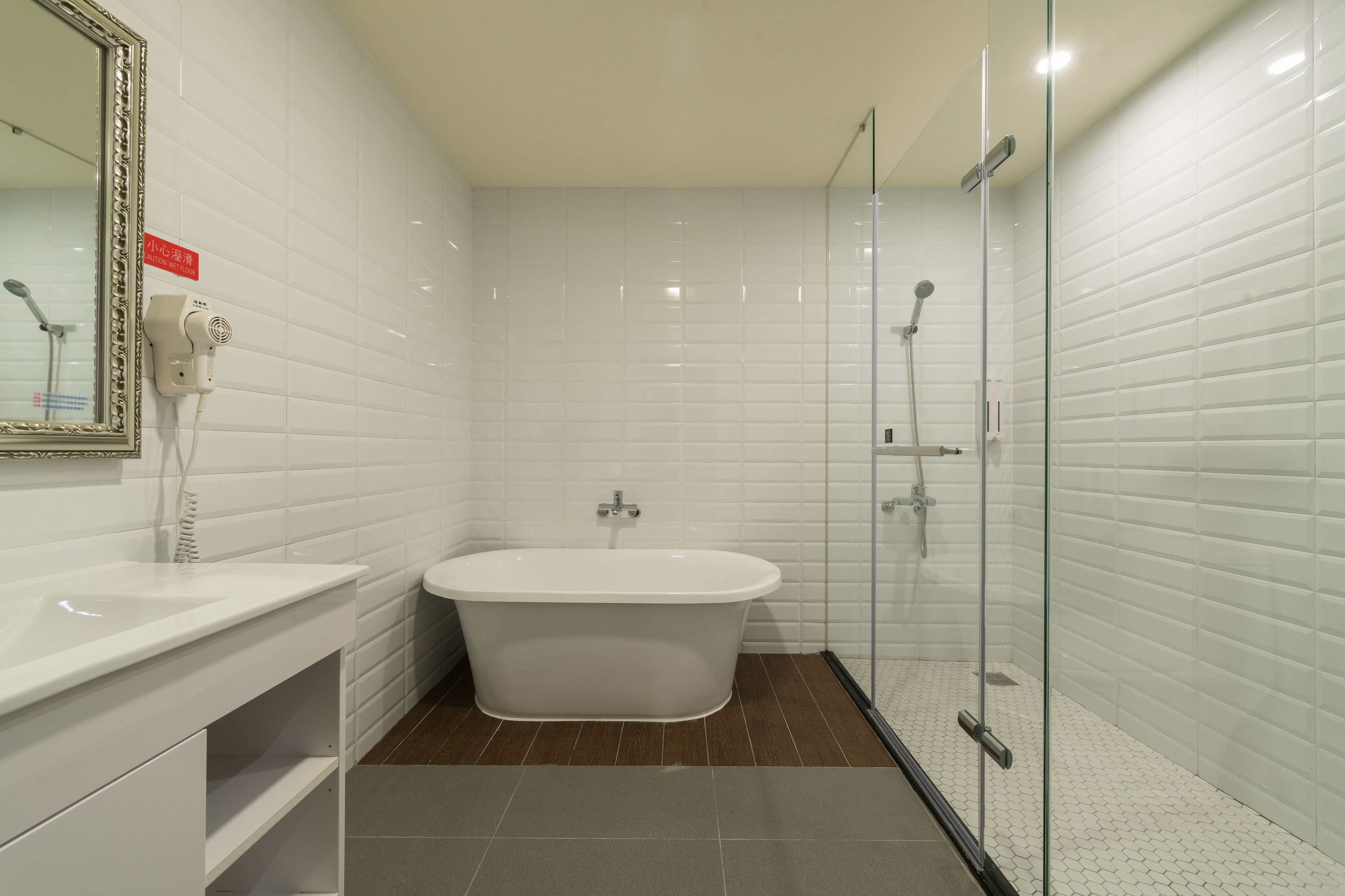 A modern bathroom with a freestanding bathtub, a glass-enclosed shower, and a white tiled wall.