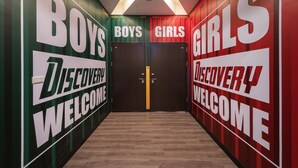 Un pasillo con letreros que dicen 'BOYS' y 'GIRLS' en paredes opuestas, que conduce a una puerta.