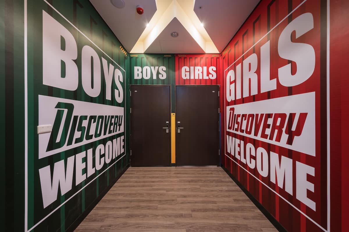 Un pasillo con letreros que dicen 'BOYS' y 'GIRLS' en paredes opuestas, que conduce a una puerta.