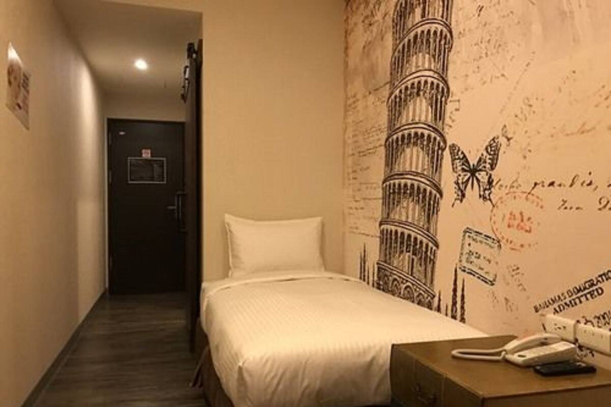 Una habitación de hotel con una cama, una mesita de noche con teléfono y una pared decorada con un diseño de torre.