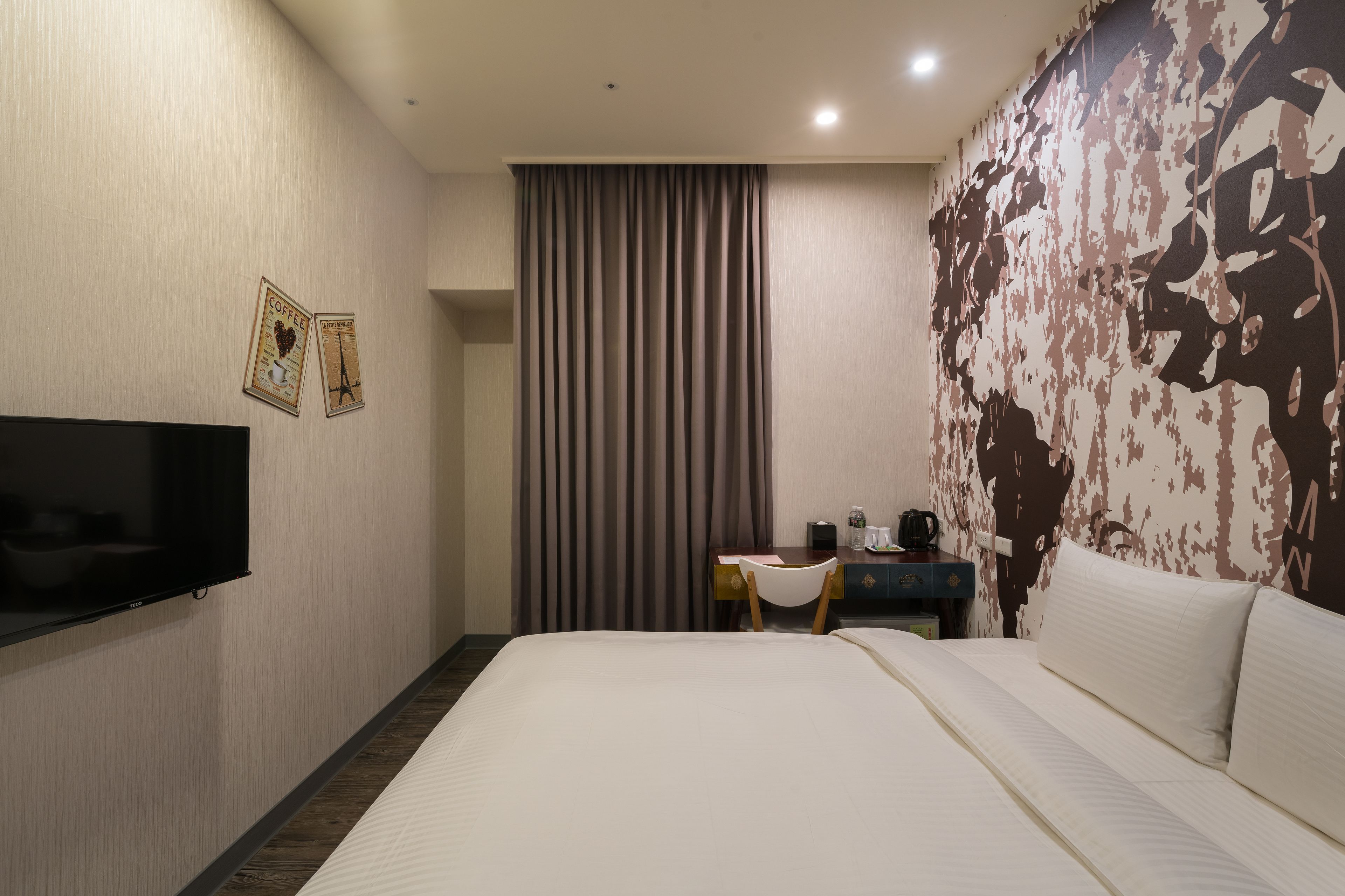 A hotel room with a bed, a desk, a chair, a flat-screen TV, and a wall with a patterned design.