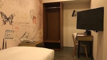 A hotel room with a bed, a desk with a chair, a television, and a wardrobe.