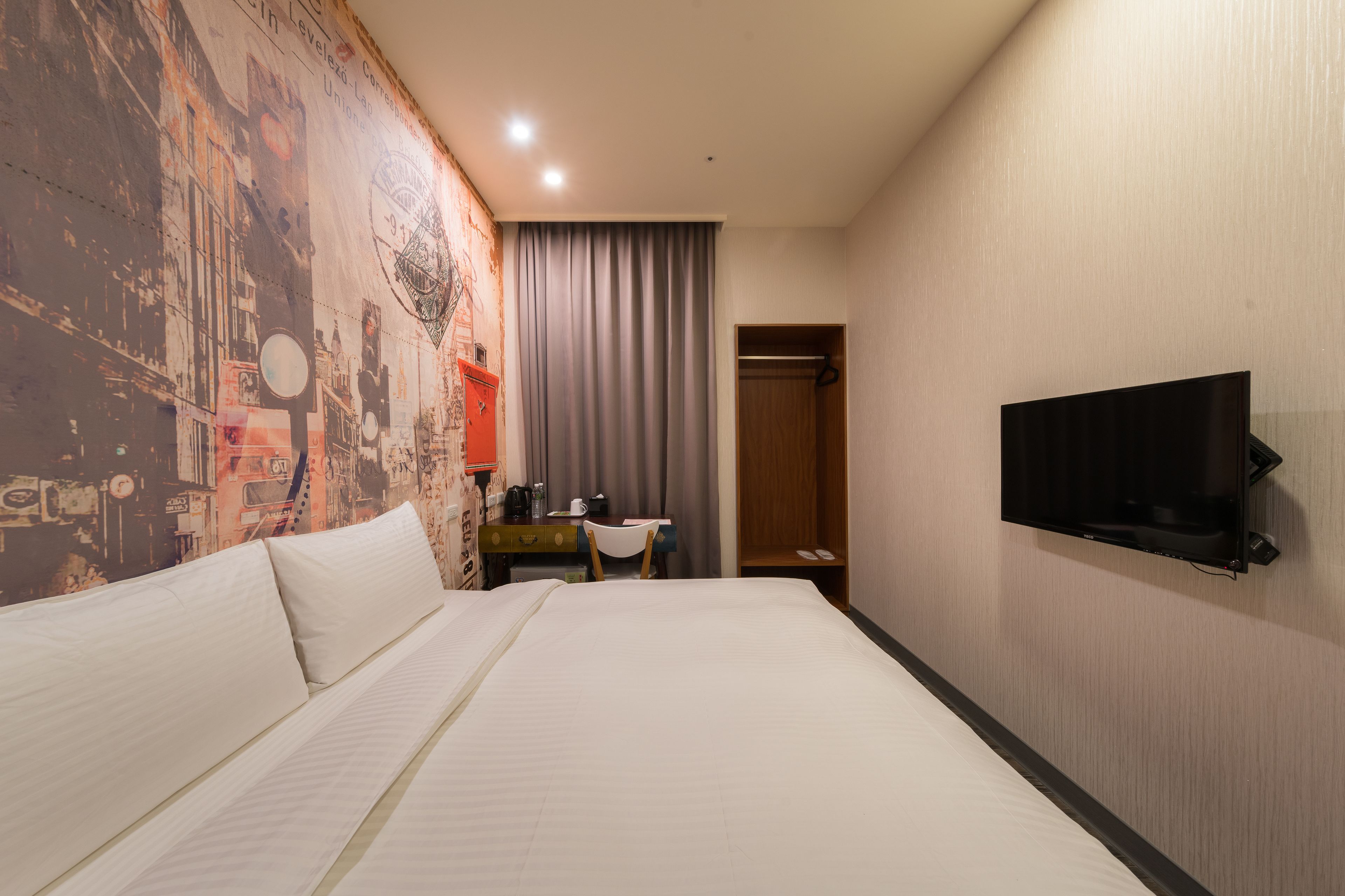 Una habitación de hotel con una cama grande, un escritorio con silla, un televisor en la pared y un armario.