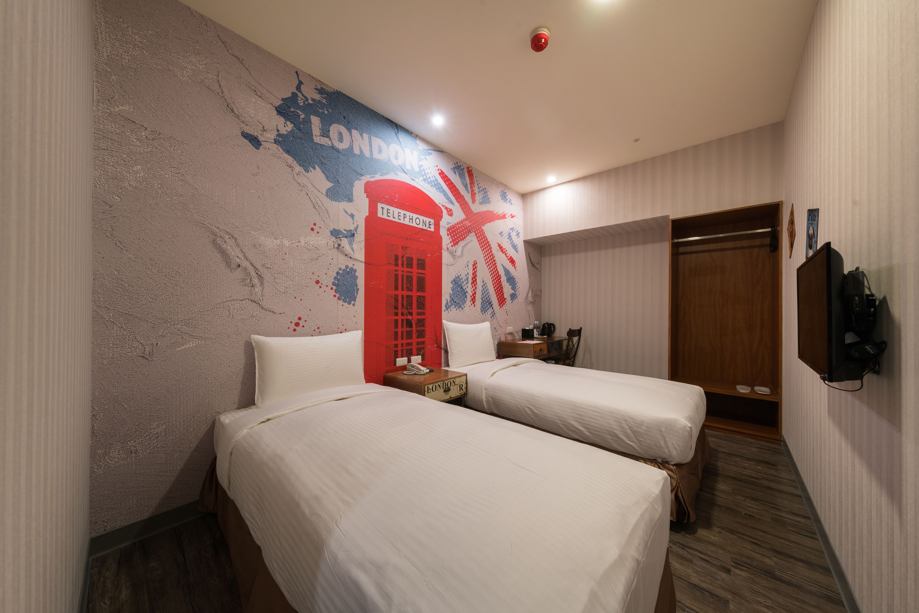 A hotel room with two beds, a wall mural of a red telephone booth, and a wooden wardrobe.
