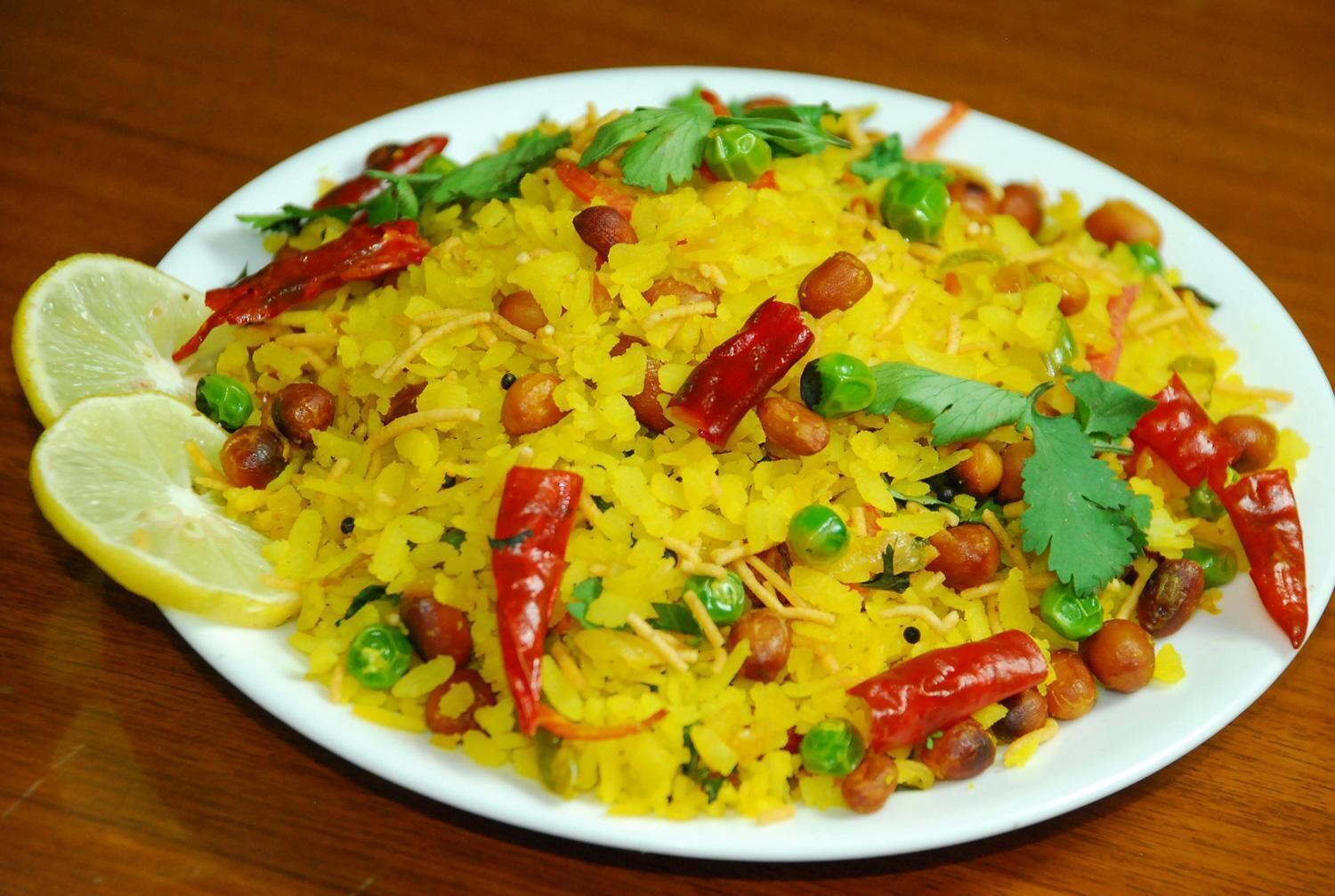 Um prato de arroz amarelo com ervilhas, amendoins e pimentas vermelhas, guarnecido com coentro e uma fatia de limão.