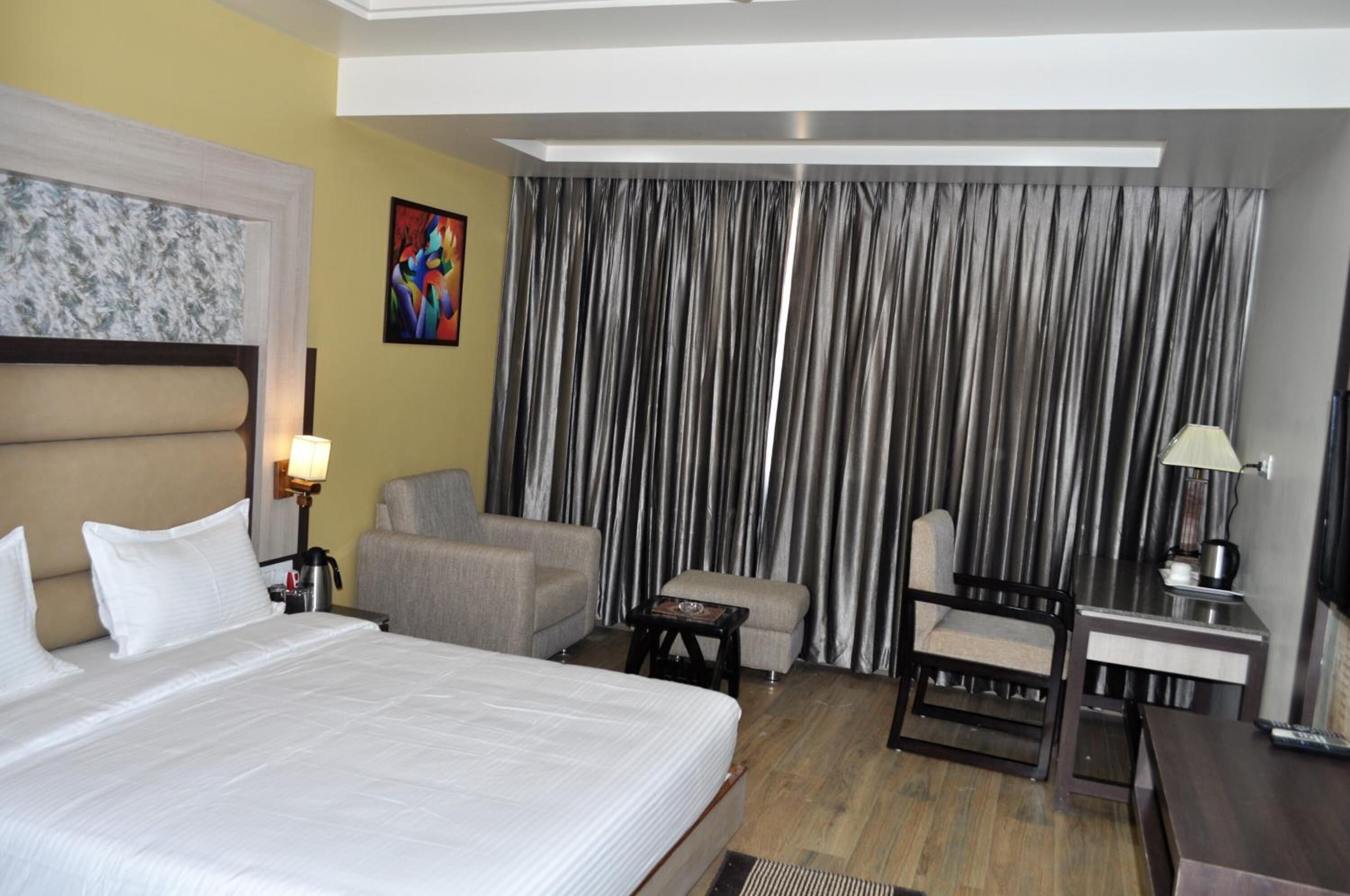 Ein Hotelzimmer mit einem Bett, einem Schreibtisch, einem Sessel und einem Sofa, sowie einem großen Fenster mit Vorhängen.